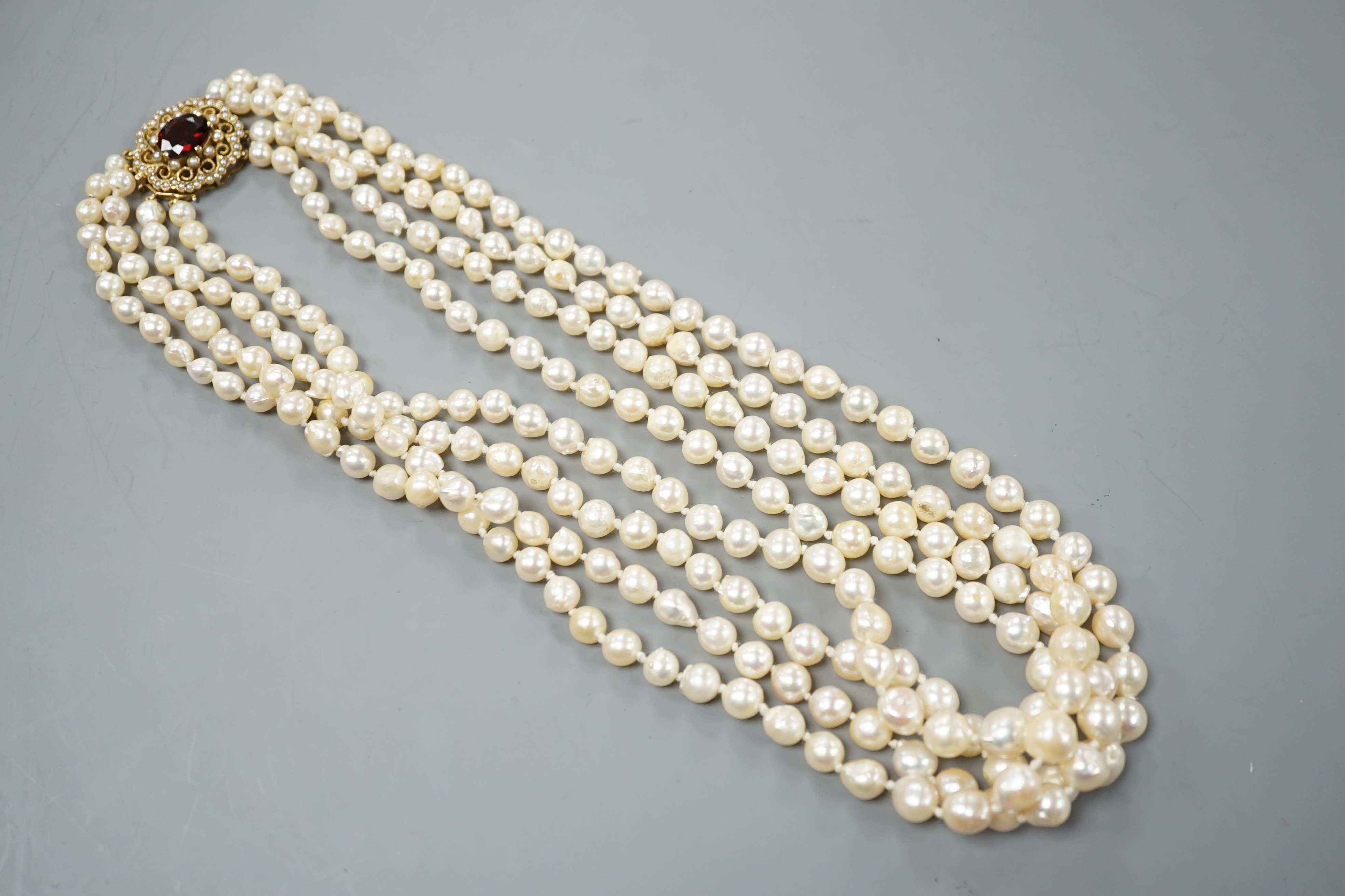 A 1960's triple strand cultured pearl necklace, with garnet and seed pearl set 9ct gold clasp, 48cm.